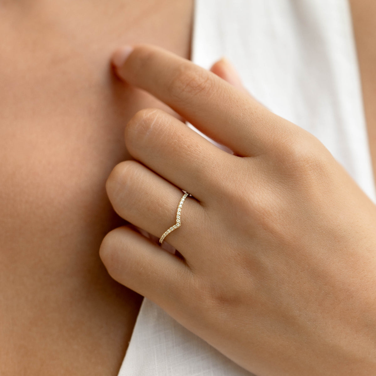 Close-up of a hand wearing the Diamond V Ring 14k Gold - Sanne with pavé diamonds on a soft neutral background