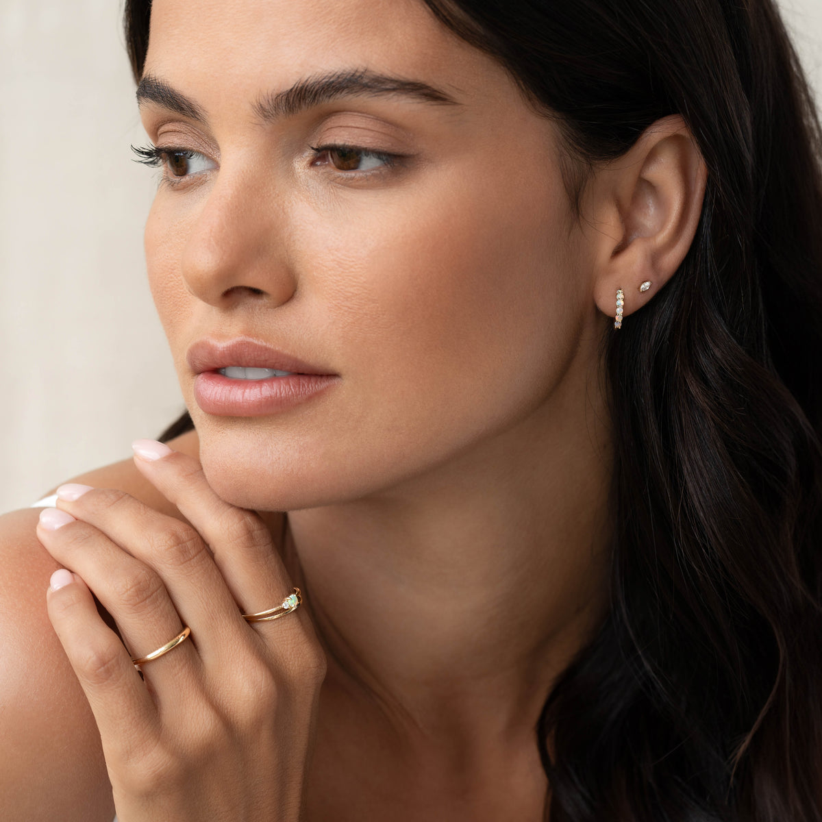 Close-up of a woman wearing Opal Huggie Earrings 14k Gold - Calypso with minimalist gold rings and soft natural light