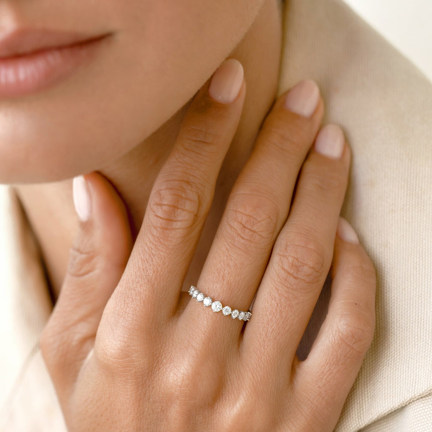 Close-up of a hand wearing the Graduated Diamond Ring White Gold - Giselle with 11 round diamonds on a light beige background