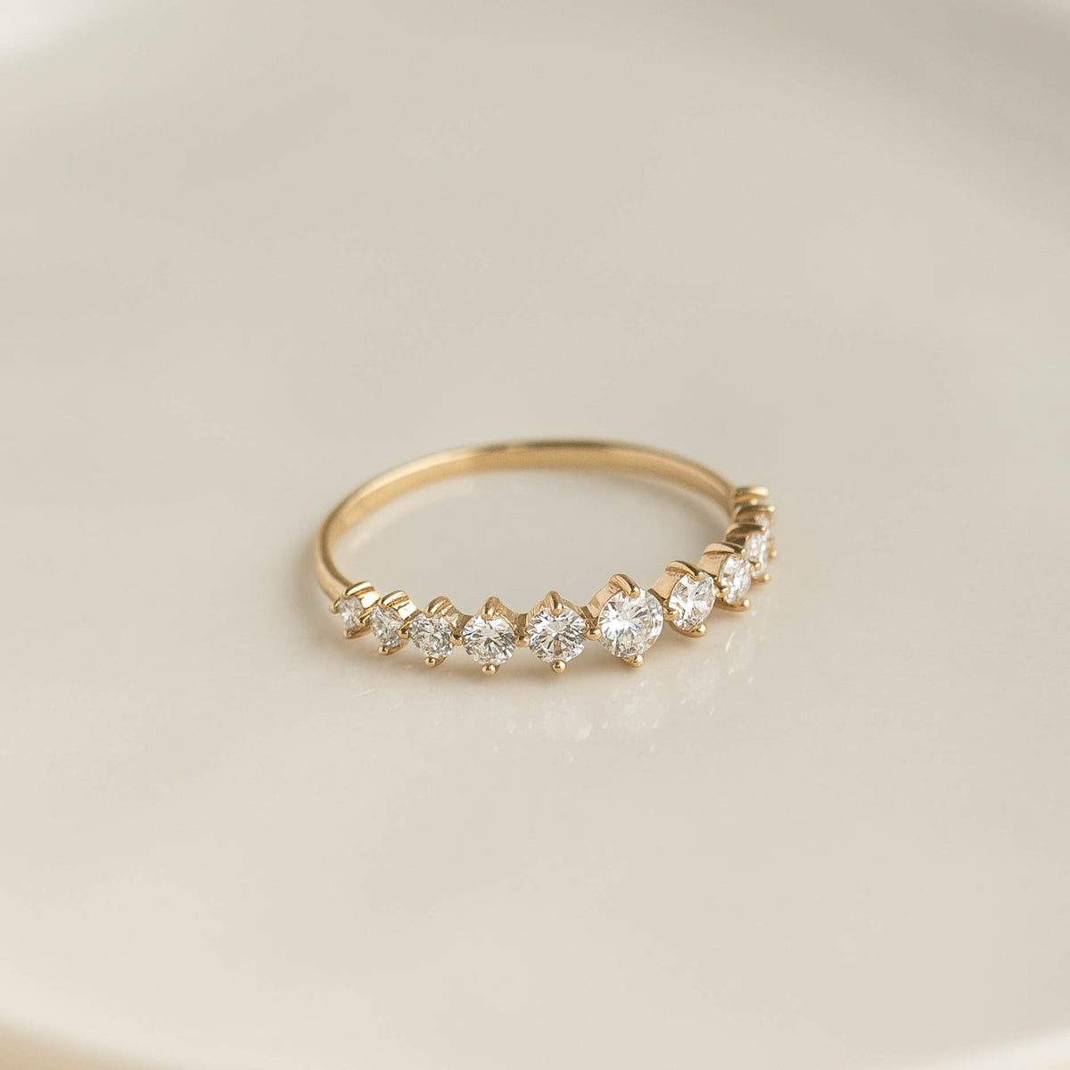 Close-up of Graduated Diamond Ring 14k Gold - Giselle featuring 11 round diamonds on a gold band on beige background