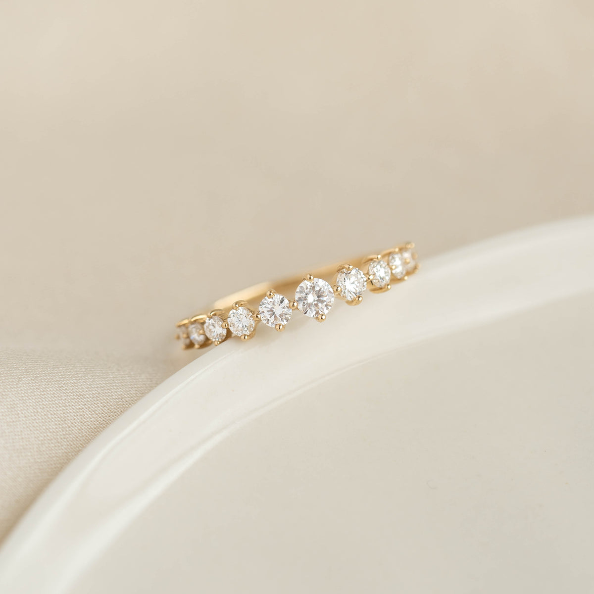 Close-up of the Graduated Diamond Ring 14k Gold - Giselle with 11 round diamonds on a gold band against a beige background