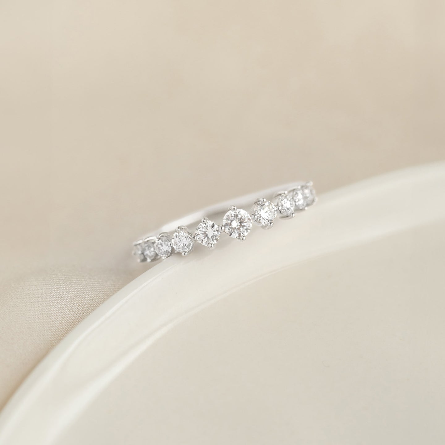 Close-up of the Graduated Diamond Ring White Gold - Giselle with 11 round diamonds on a white gold band on beige background