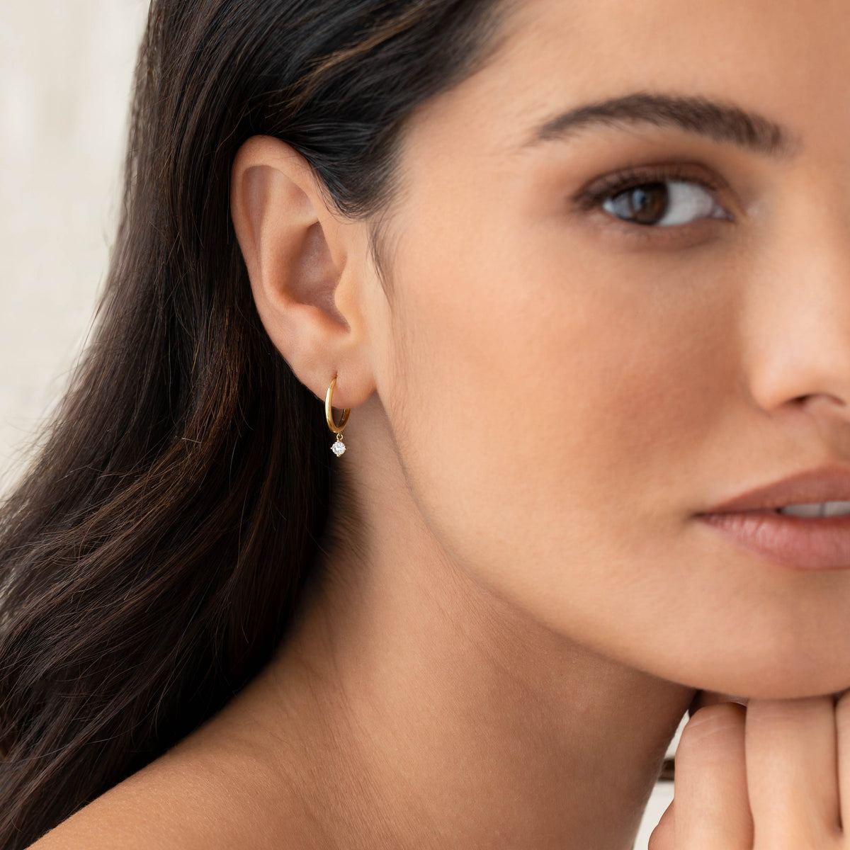 Close-up of a woman wearing Diamond Drop Huggie Earrings 14k Gold - Joleen with delicate diamond drops and gold hoops