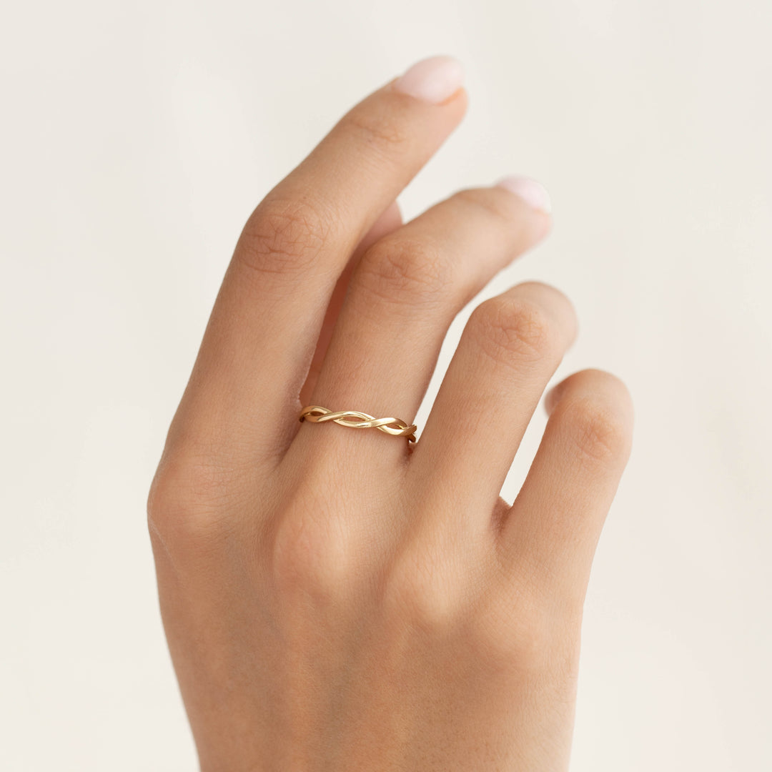 Close-up of a hand wearing the Twist Ring 14k Gold - Liana showcasing two intertwining bands on a light background