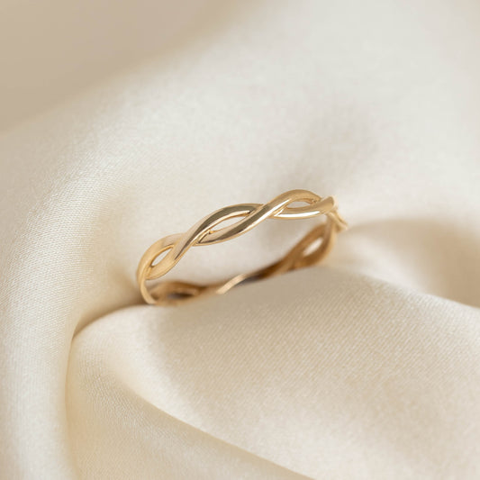 Close-up of the Twist Ring 14k Gold - Liana with two intertwining bands on soft beige fabric background