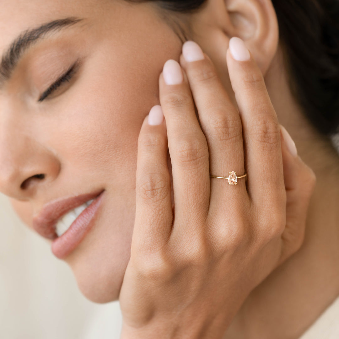 Woman with eyes closed wearing Pear Shaped Morganite Ring 14k Gold - Martine on her ring finger near face