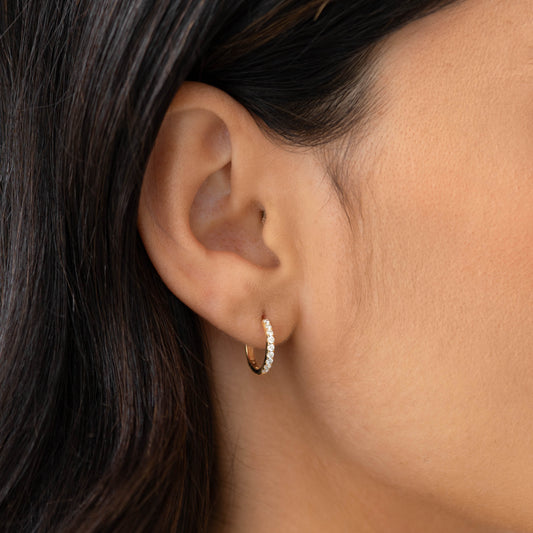 Close-up of a woman wearing Pave Diamond Huggie Earrings 14k Gold - Oceane with 18 pavé set diamonds on ear