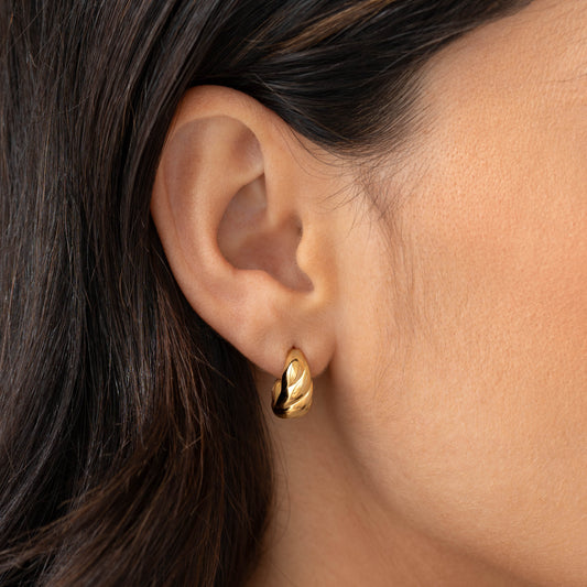 Close-up of a gold vermeil Croissant Earrings - Piper worn on the ear against a neutral background