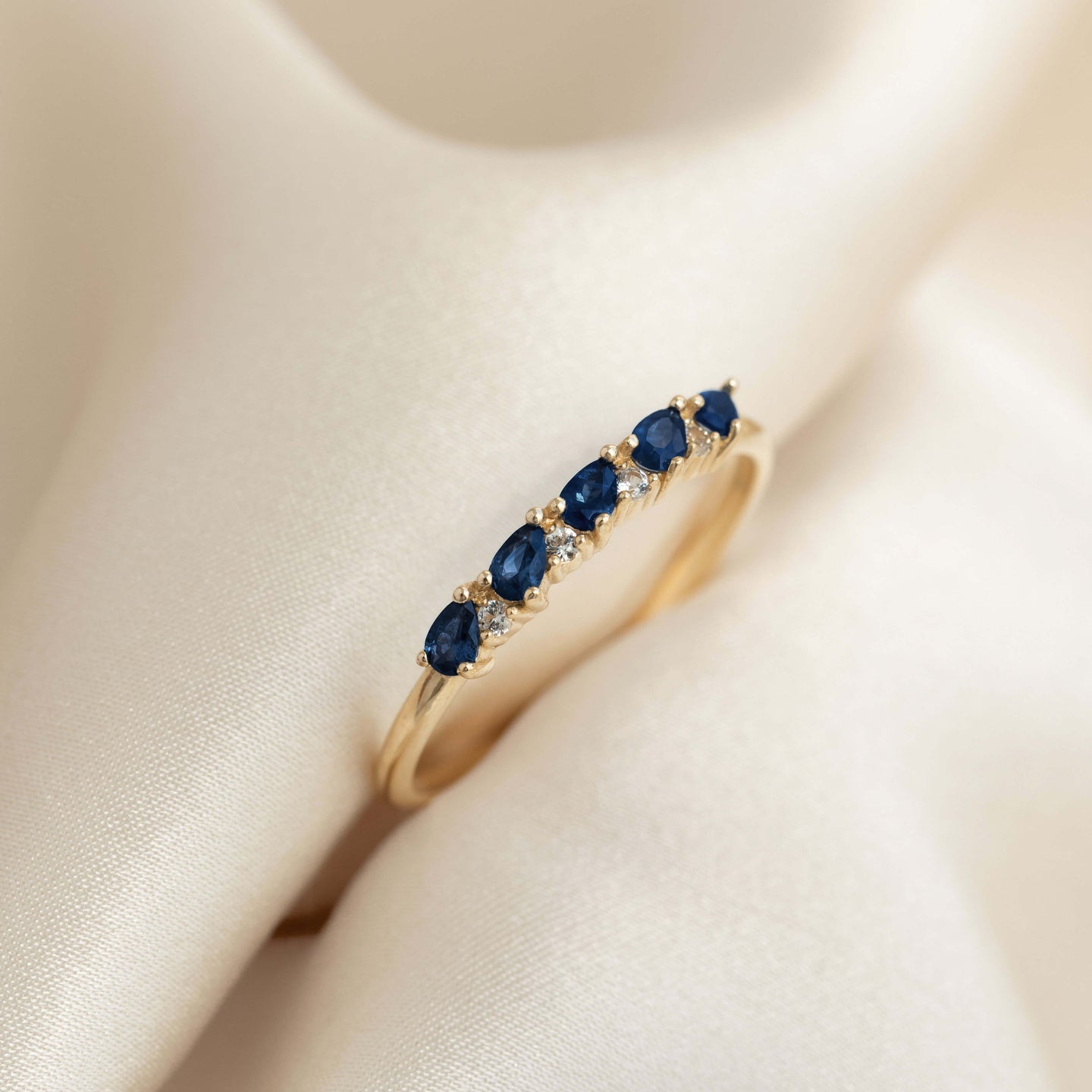 Close-up of Sapphire Half Eternity Ring 14k Gold - Capriana with pear-cut blue sapphires and round white sapphires on cream fabric
