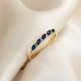 Close-up of Sapphire Half Eternity Ring 14k Gold - Capriana with pear-cut blue sapphires and round white sapphires on cream fabric