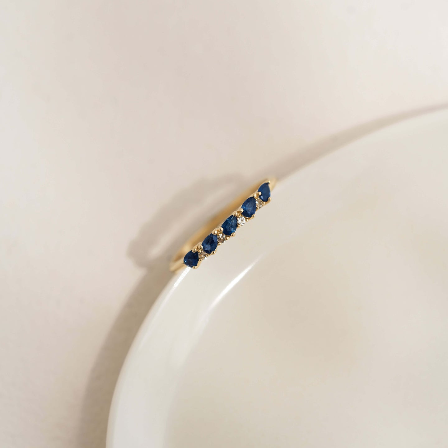 Sapphire Half Eternity Ring 14k Gold - Capriana with pear-cut blue sapphires on a white curved surface