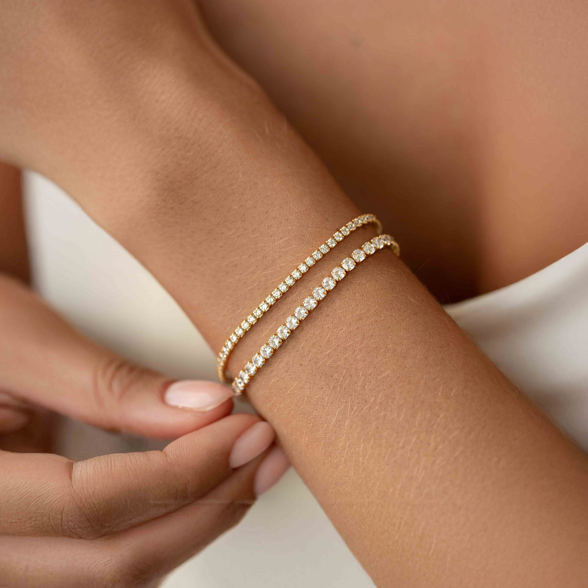 Close-up of a wrist adorned with two delicate Tennis Bracelet - Zilla pieces featuring round cubic zirconia stones and gold vermeil