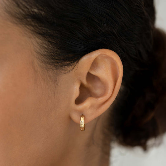 Close-up of a woman wearing Gold Hammered Huggie Hoop Earrings - Yulla with a textured gold finish and hinge back closure