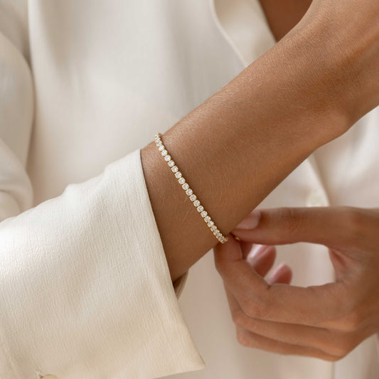 Close-up of a hand wearing the Tennis Bracelet - Zilla with gold vermeil and cubic zirconia stones on a light fabric sleeve