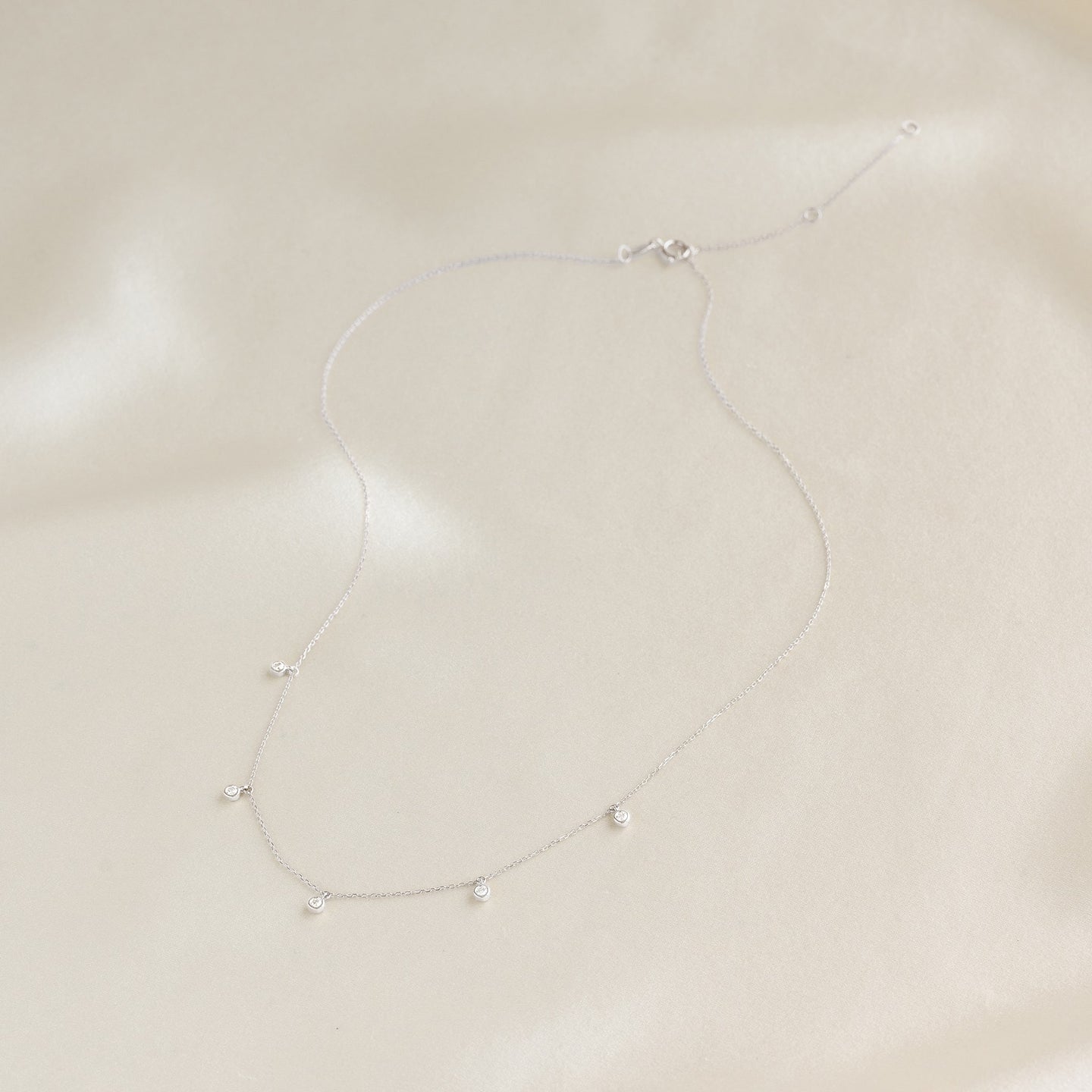 5-Diamond Necklace White Gold - Bette featuring five bezel-set diamonds on a delicate white gold chain on cream fabric background