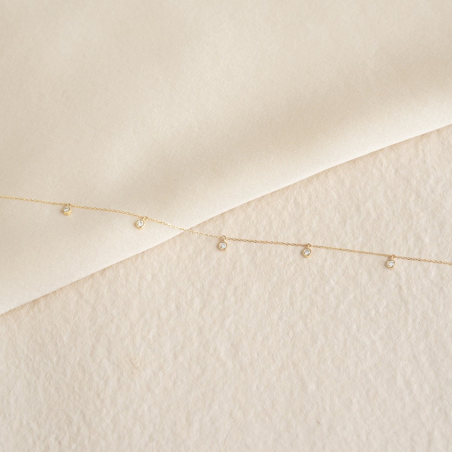 Delicate 5-Diamond Necklace 14k Gold - Bette with five bezel-set diamonds on a fine gold chain on textured background