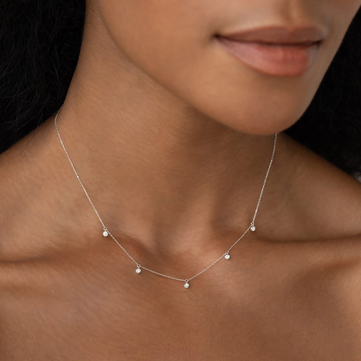 Close-up of a woman wearing the 5-Diamond Necklace White Gold - Bette with five bezel-set diamonds on a delicate chain