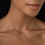 Close-up of a 5-Diamond Necklace 14k Gold - Bette with five bezel-set diamonds on a woman’s neck against soft background