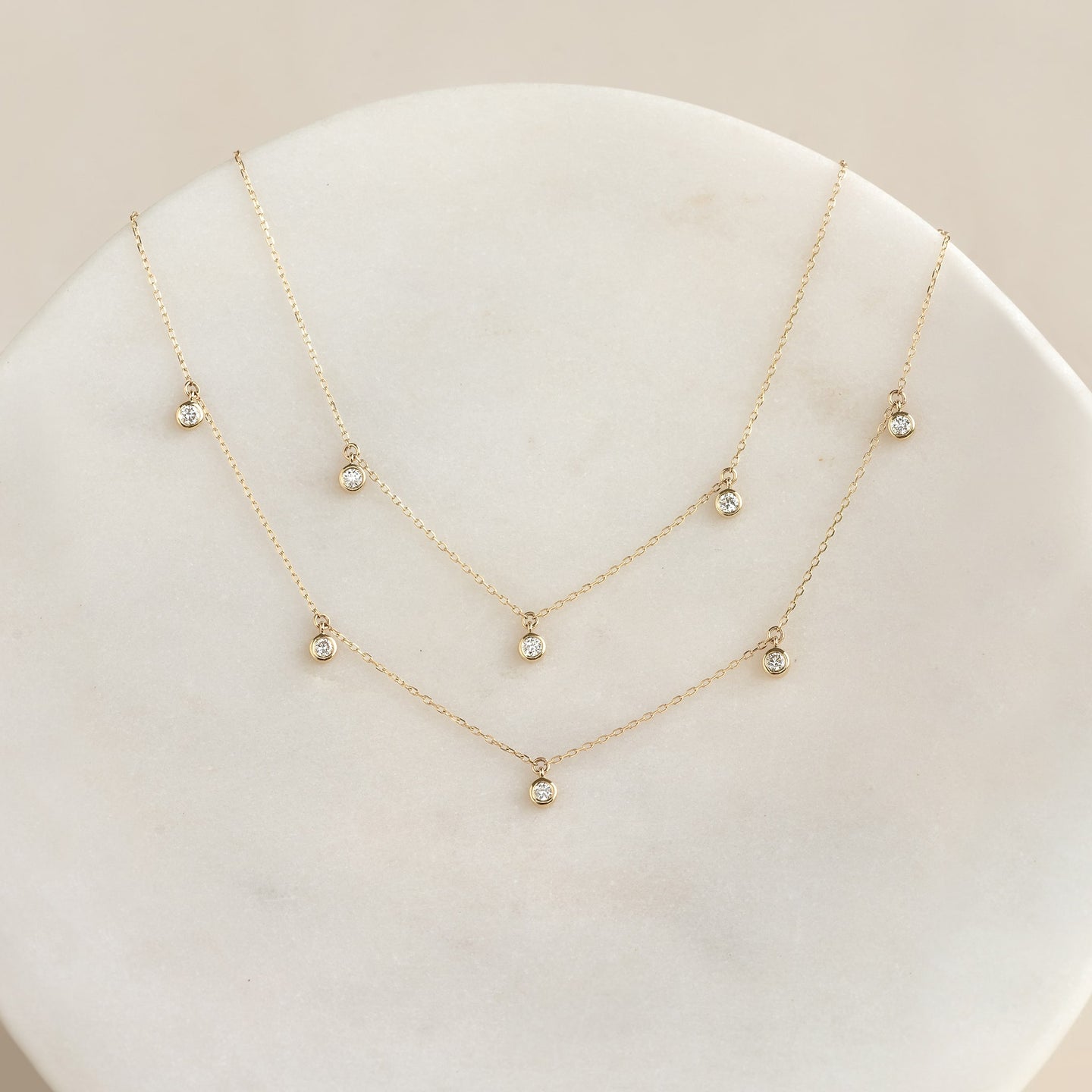 Close-up of three delicate 3-Diamond Necklace 14k Gold - Eira pieces with bezel-set stones on a light background