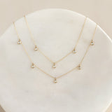 Close-up of three delicate 3-Diamond Necklace 14k Gold - Eira pieces with bezel-set stones on a light background