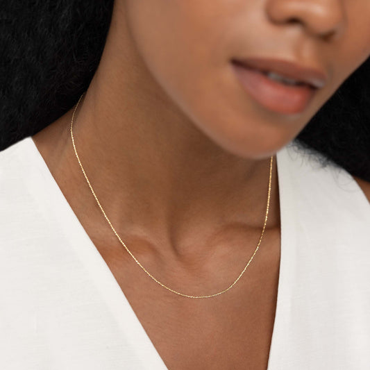 Close-up of a woman wearing a Tinsel Chain Necklace 14k Gold - Embla with a white blouse and soft natural light