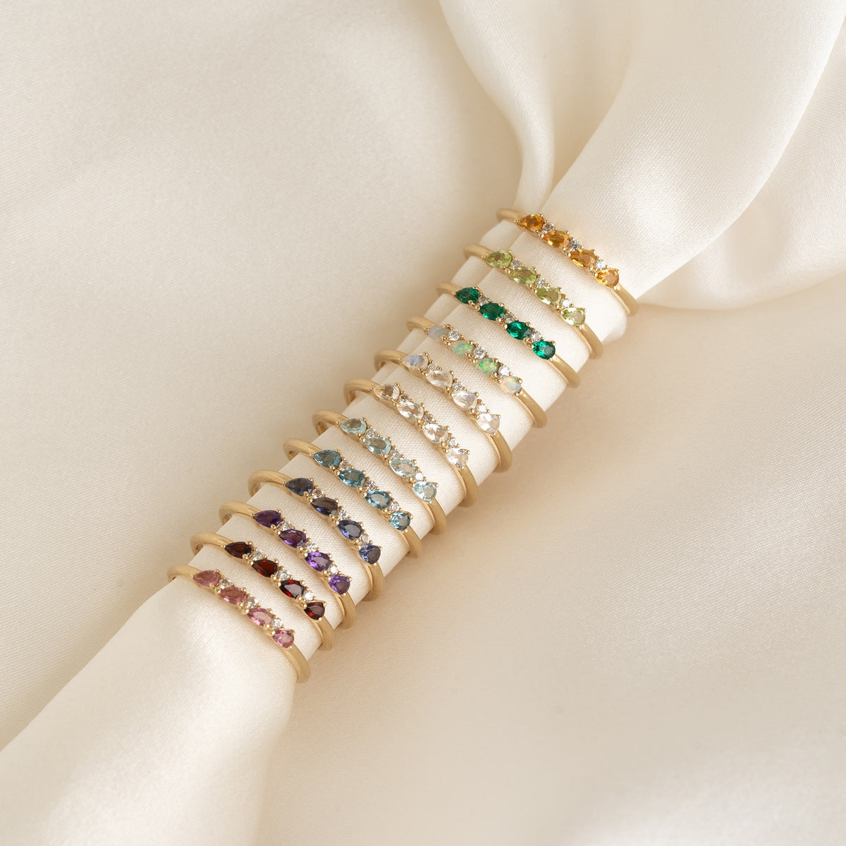 Row of delicate gold rings featuring various colored gemstones on white fabric, showcasing March Birthstone Pear Ring 14k Gold - Swiss Blue Topaz and Diamond