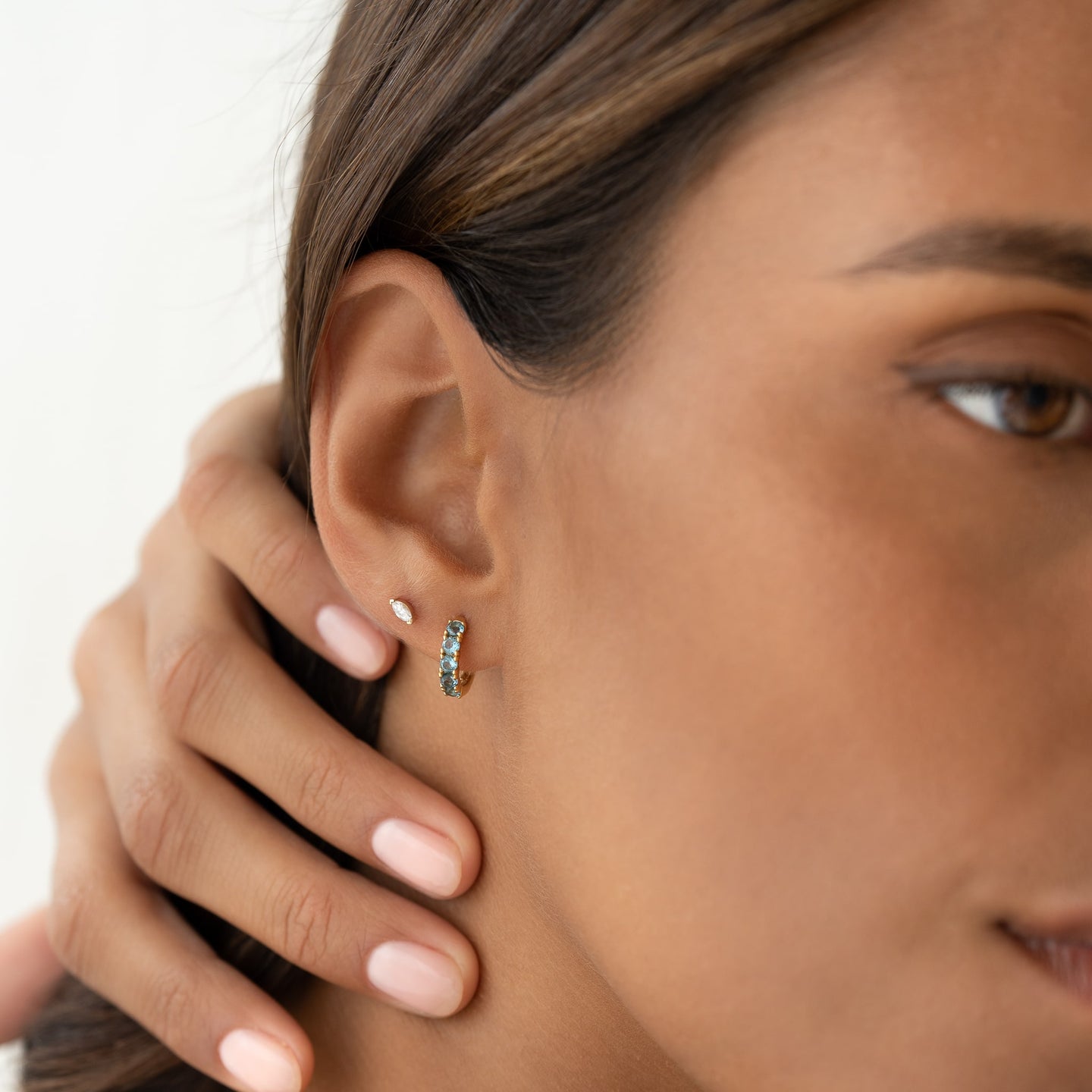Close-up of a woman wearing September Birthstone Huggie Earrings - London Blue Topaz with gold vermeil setting on a neutral background