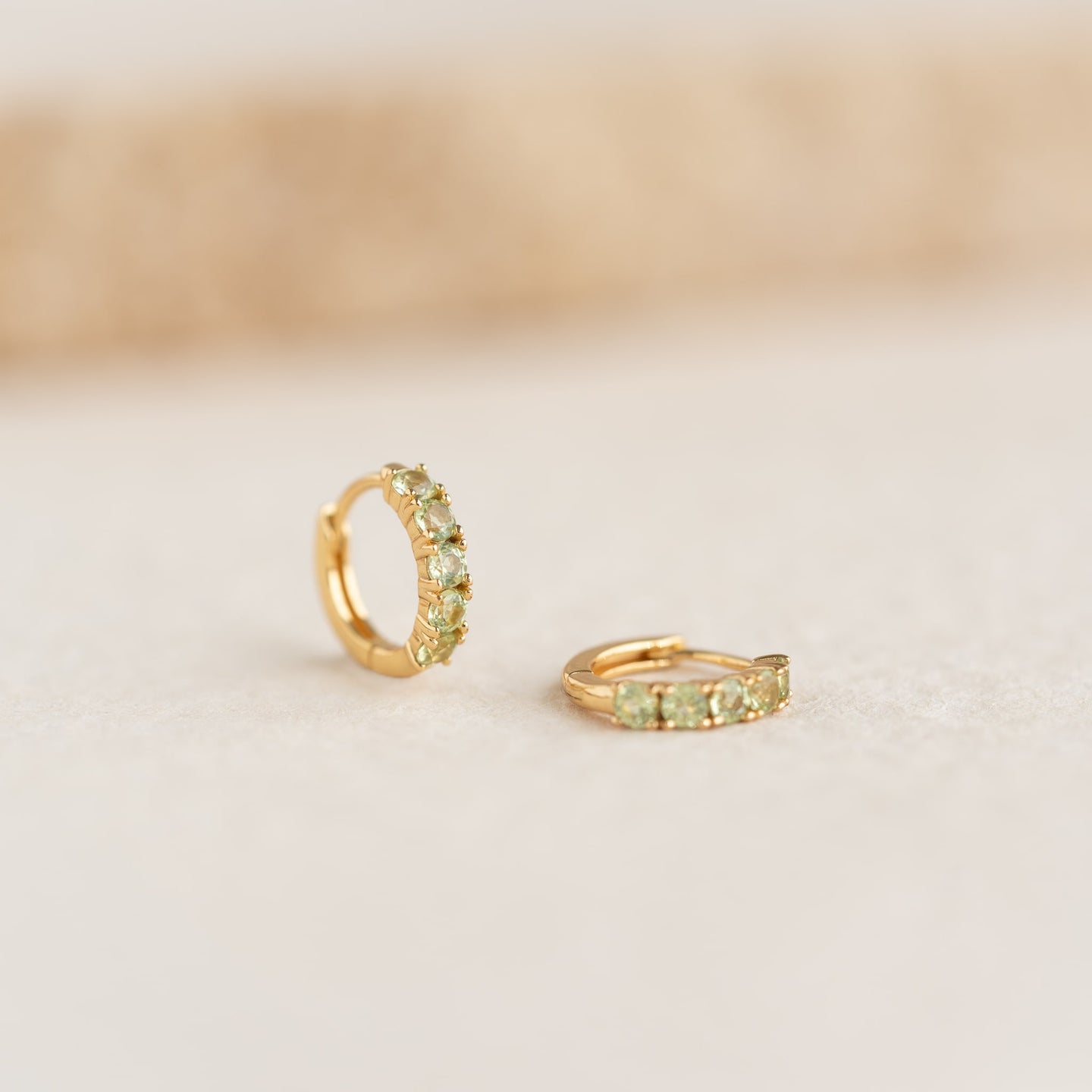 Close-up of August Birthstone Huggie Earrings - Olivine featuring gold vermeil and vibrant olive green gemstones on neutral background