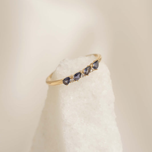Close-up of December Birthstone Pear Ring 14k Gold - Cordierite and Diamond with pear-shaped blue stones on pale background