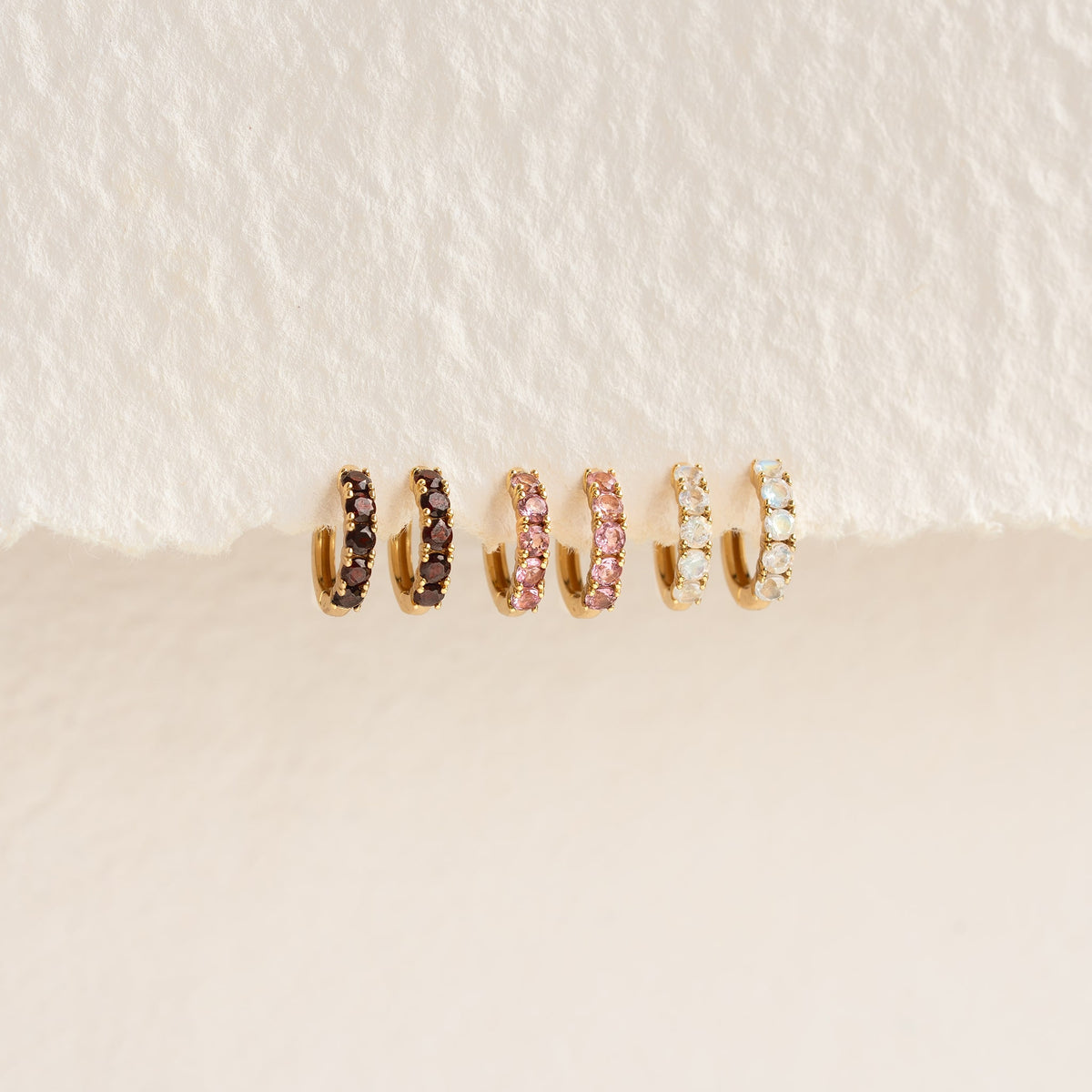 Close-up of July Birthstone Huggie Earrings - Pink Tourmaline with gold vermeil setting on a neutral background