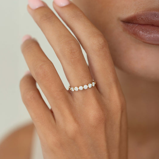 A close-up of a hand wearing a delicate Yellow Gold ring set with round diamonds.