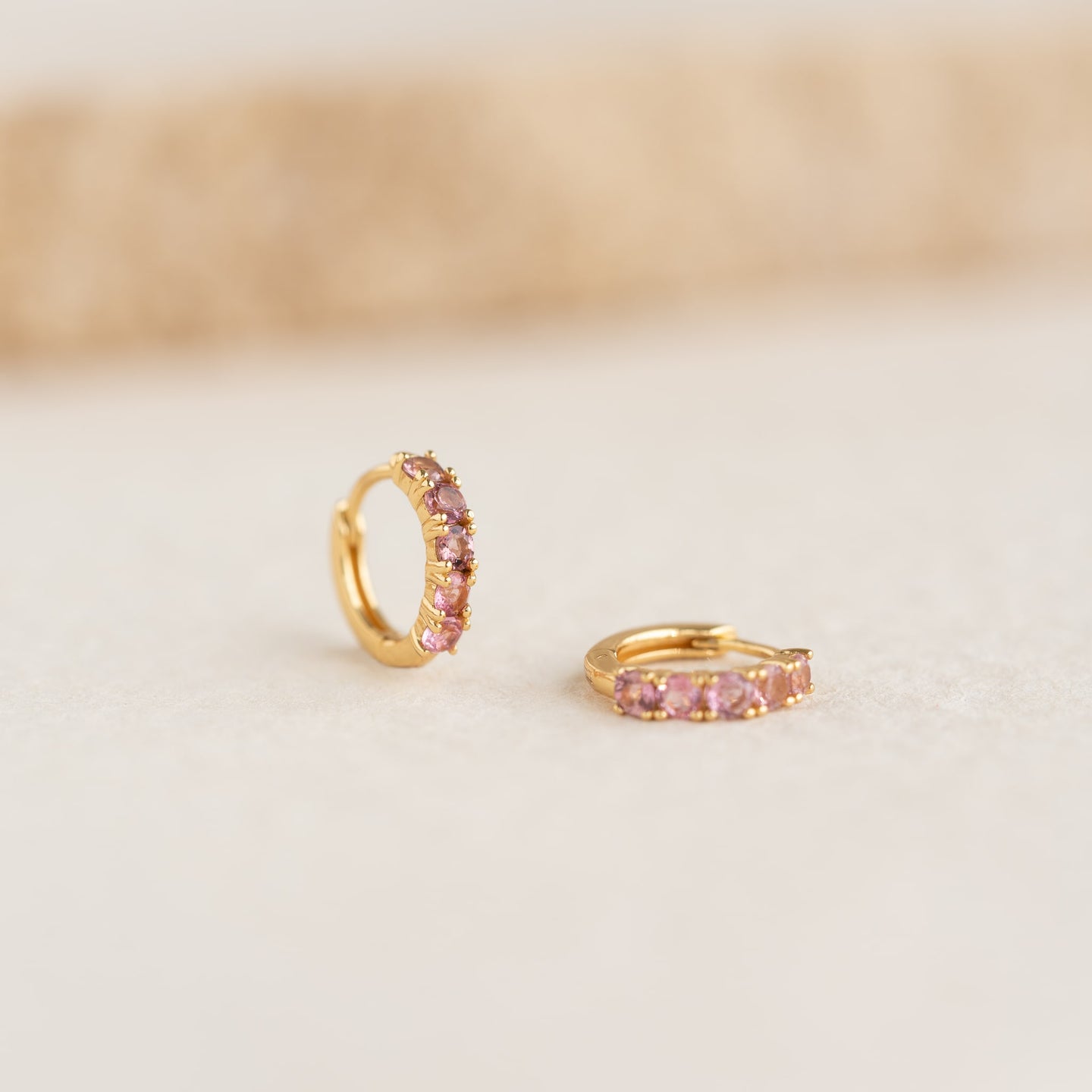 Close-up of July Birthstone Huggie Earrings - Pink Tourmaline with gold vermeil setting on neutral background