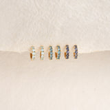 September Birthstone Huggie Earrings - London Blue Topaz in gold vermeil with varying blue gemstones on a cream background