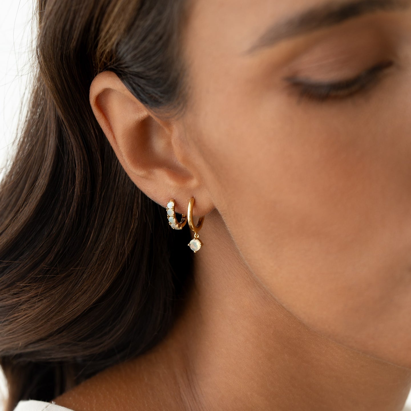 Close-up of a woman wearing October Birthstone Huggie Earrings - Opal with vibrant Ethiopian opal stones set in gold vermeil