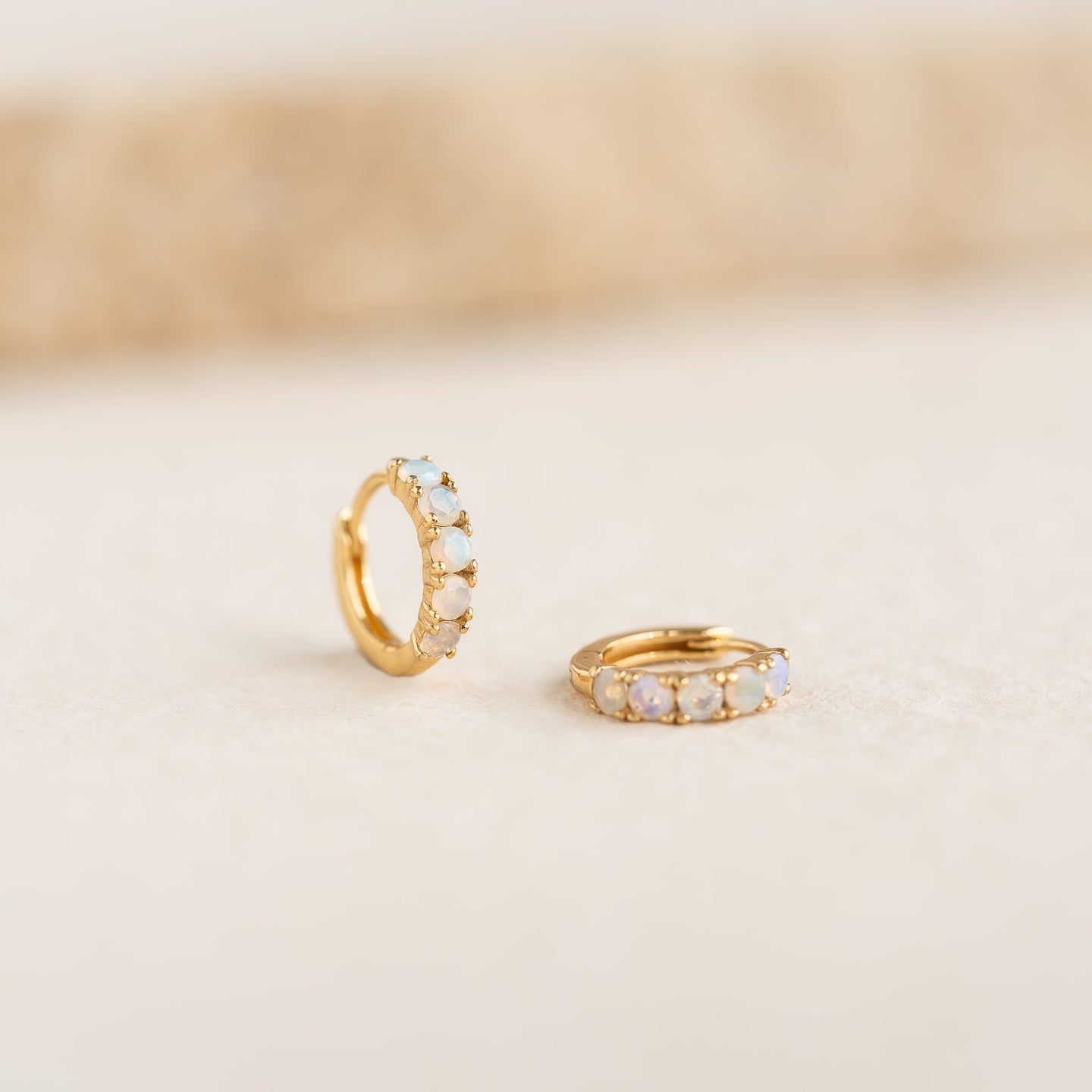 Close-up of October Birthstone Huggie Earrings - Opal featuring gold vermeil and vibrant Ethiopian opal stones on a light background