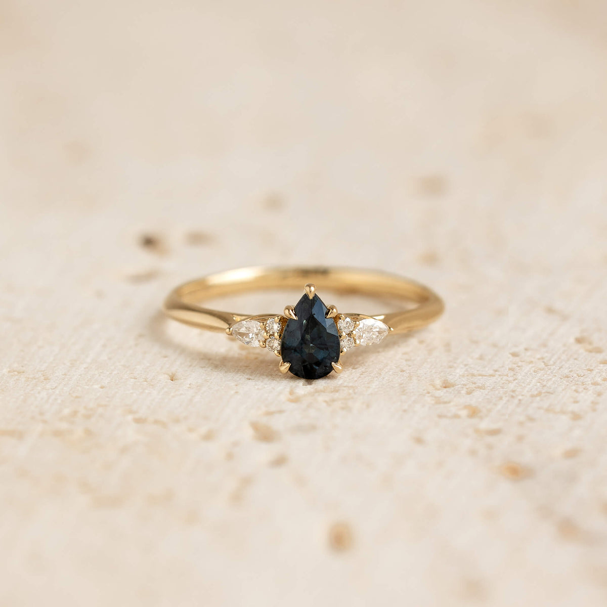 A close-up photograph displays a delicate yellow Gold ring centered against a soft, textured beige background.