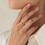 Close-up of a hand wearing the Round Rose Gold Band - Marni on the ring finger against a neutral background