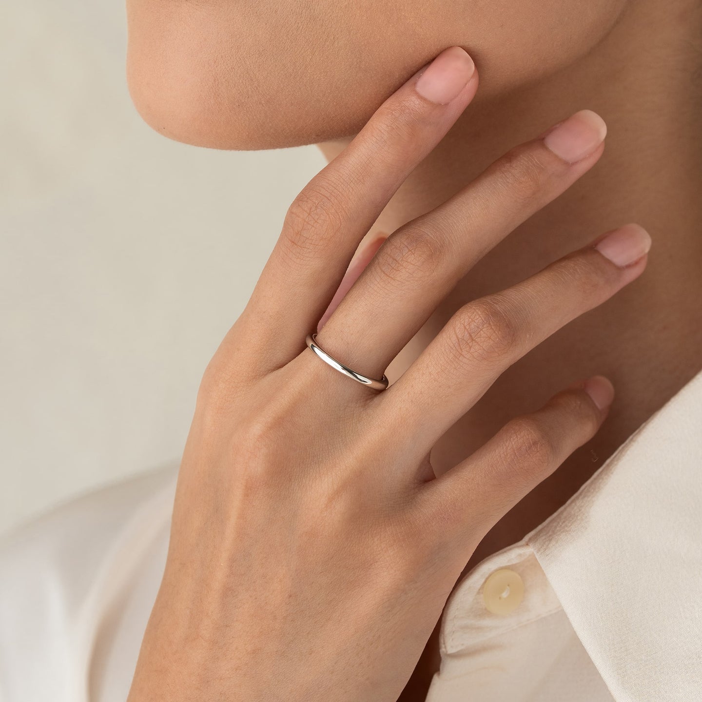 Close-up of a hand wearing the Round White Gold Band - Marni on the ring finger against a neutral background