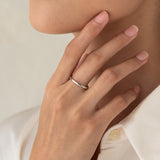 Close-up of a hand wearing the Round White Gold Band - Marni on the ring finger against a neutral background