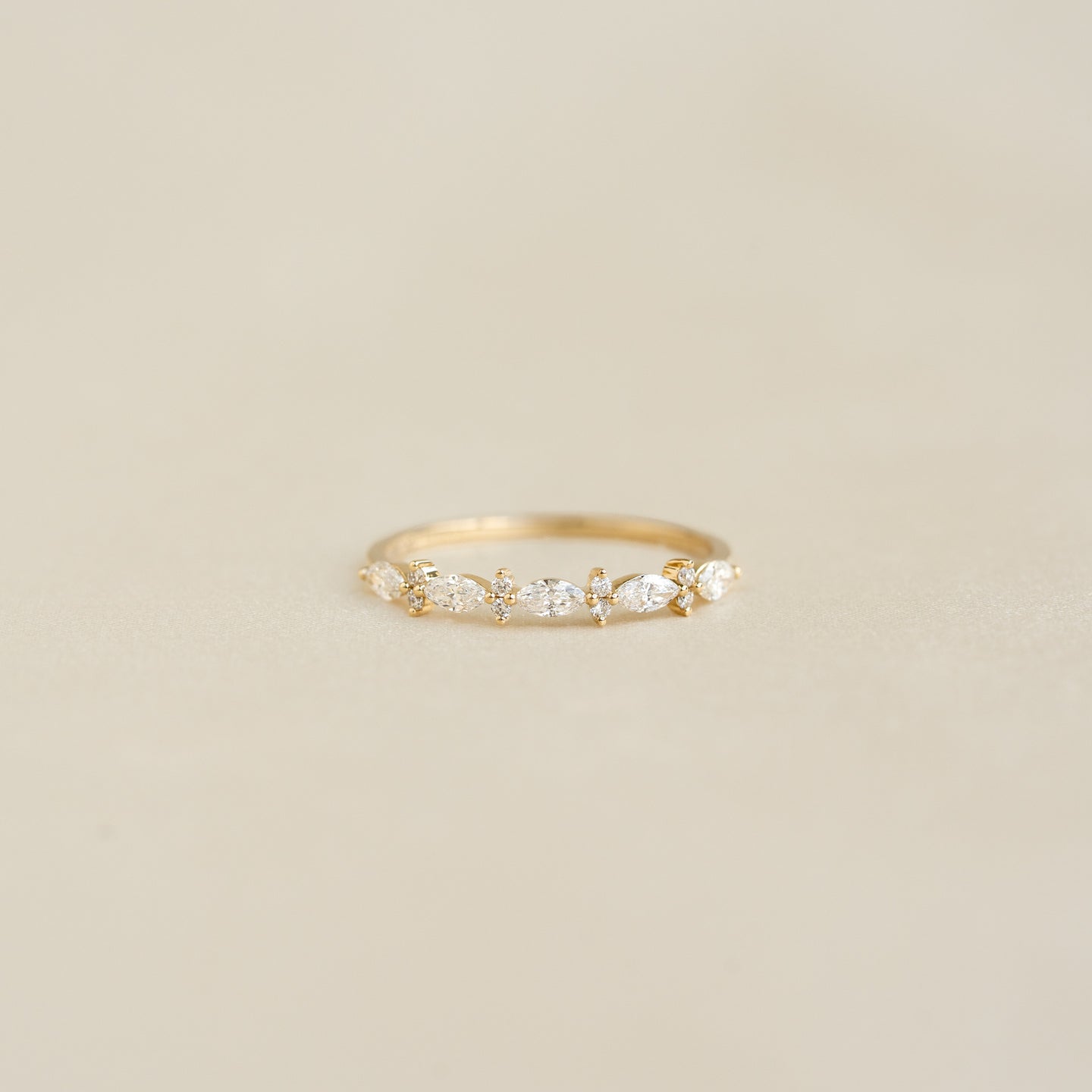 Close-up of Marquise and Round Diamond Ring - Aurelia with marquise and round diamonds on 14k yellow gold band on beige background