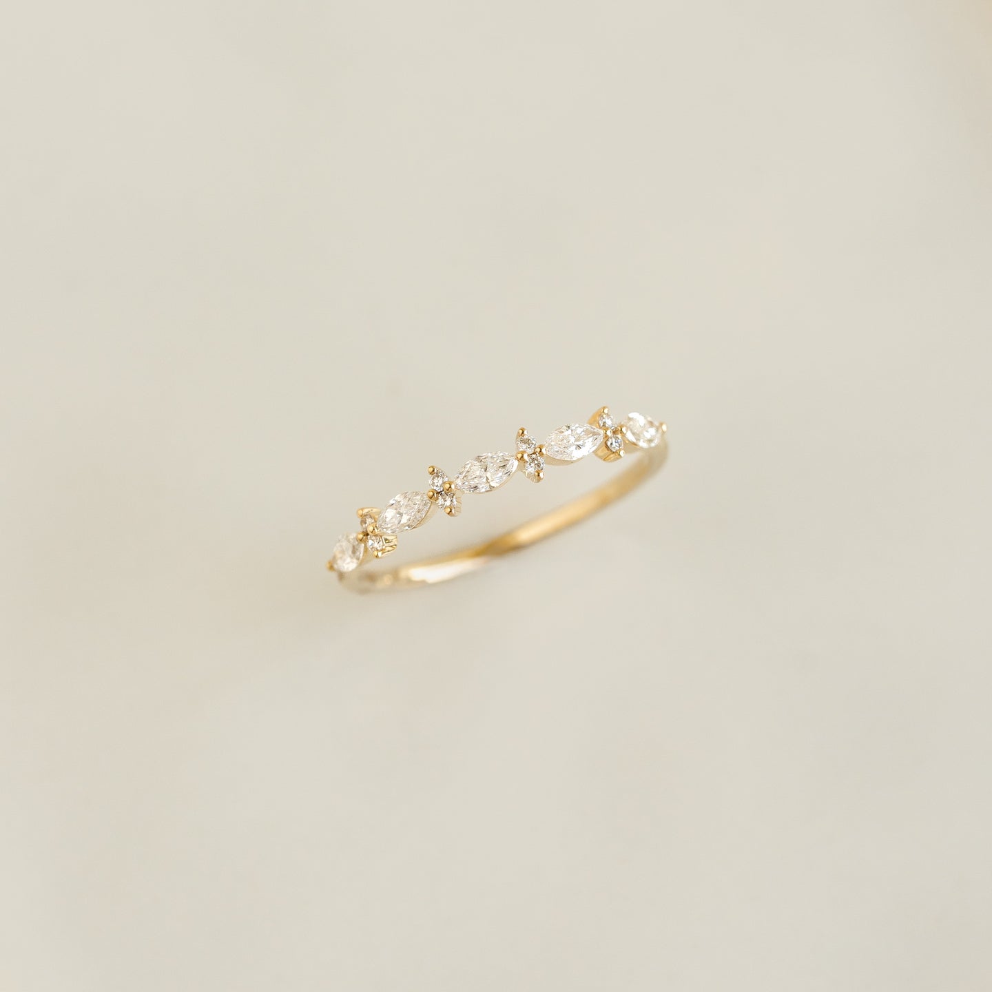 Close-up of Marquise and Round Diamond Ring - Aurelia with 14k yellow gold band on a soft beige background