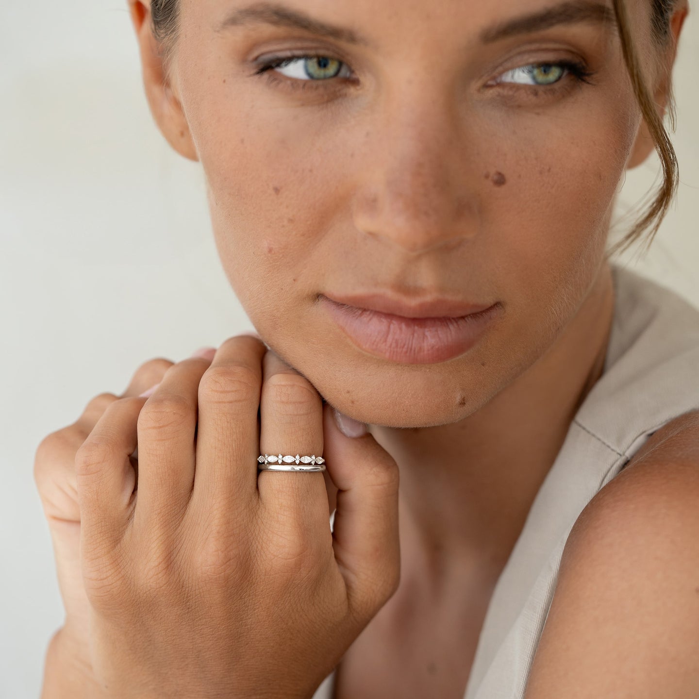 Close-up of a woman wearing the Round White Gold Band - Marni on her finger with a neutral background