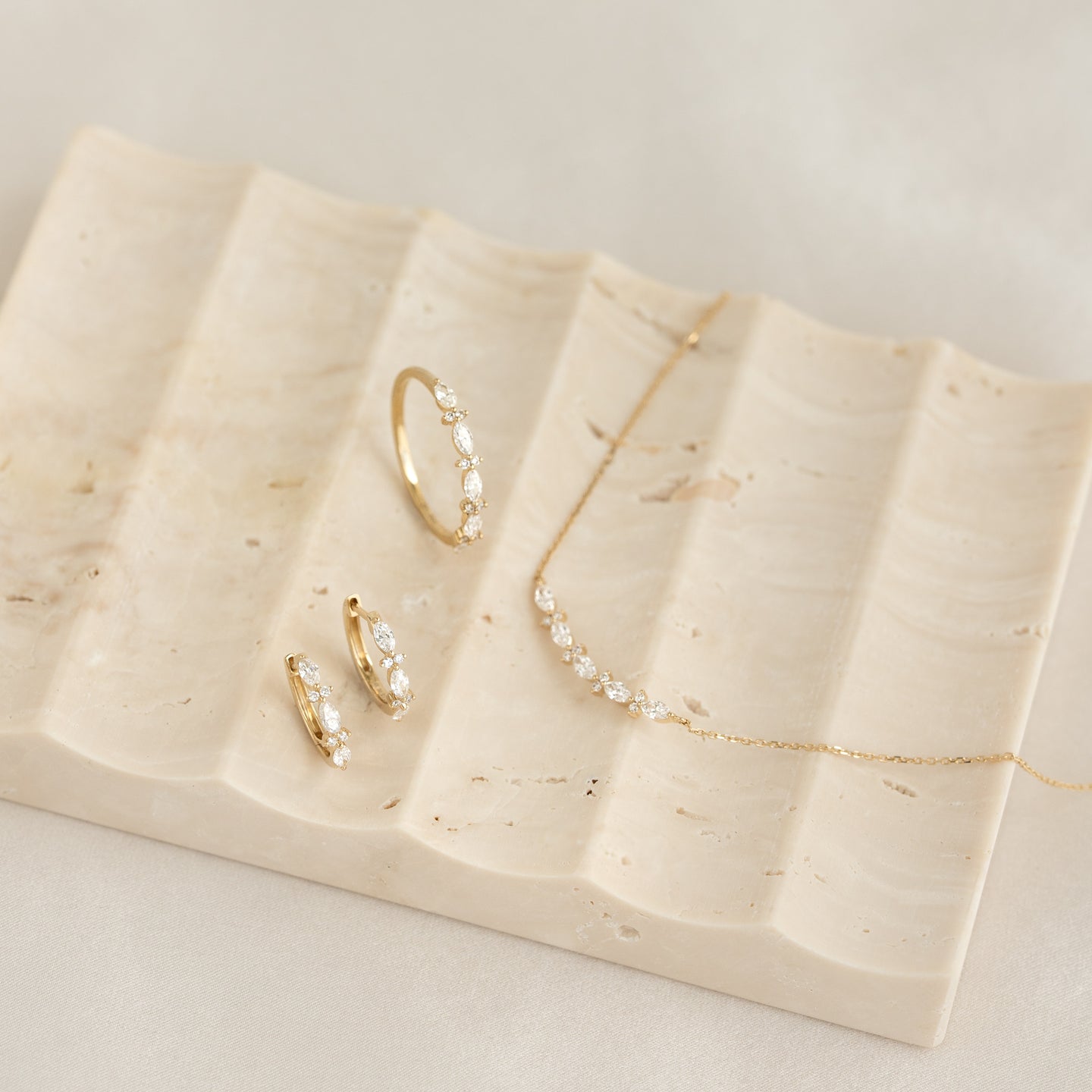 Marquise and Round Diamond Ring - Aurelia on a beige textured tray with matching gold and diamond jewelry pieces