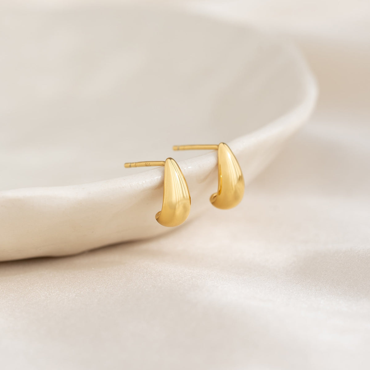 Close-up of gold vermeil tapered dome huggie earrings Brianne on soft cream fabric background