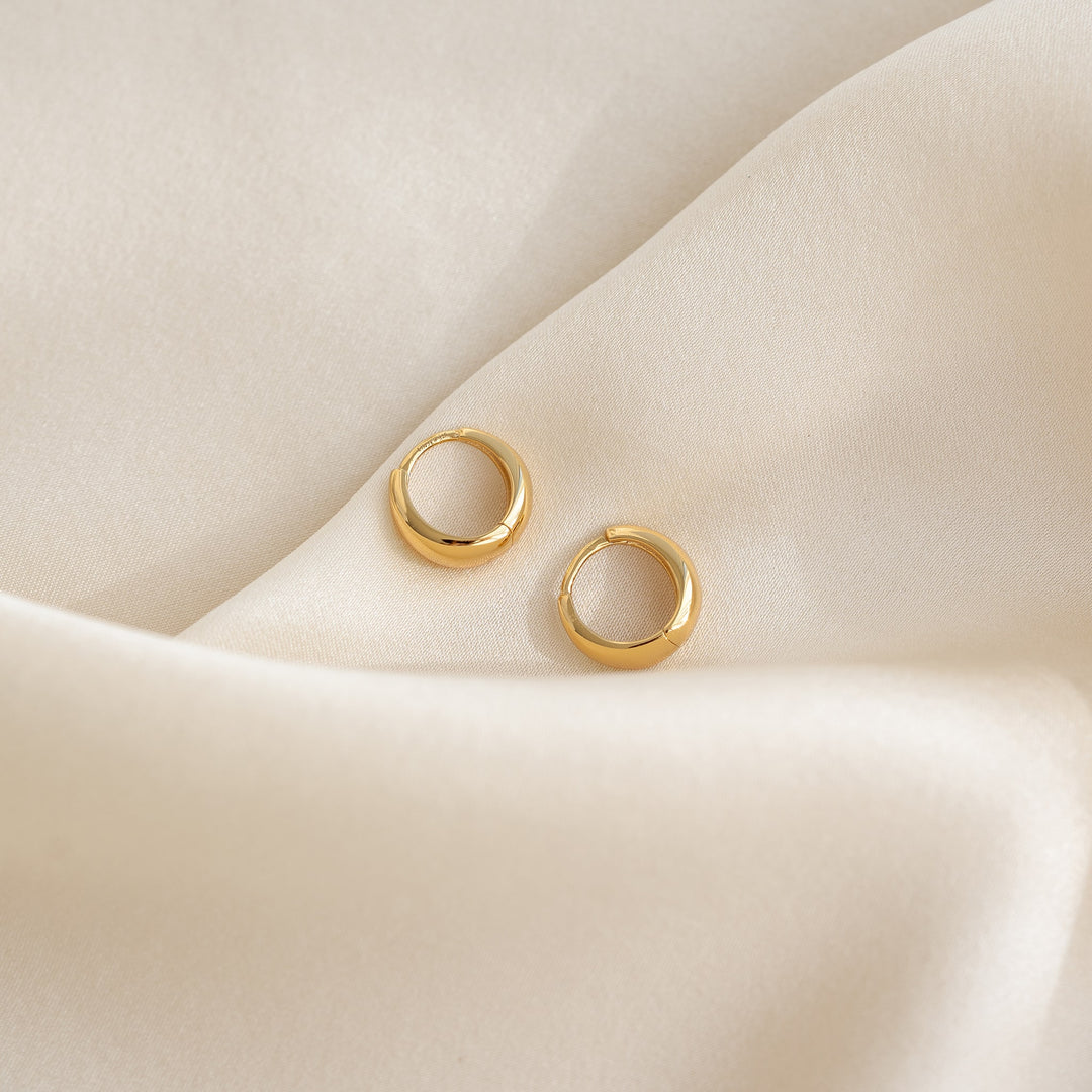 Close-up of gold vermeil Dome Huggie Earrings - Cassia resting on soft cream fabric background