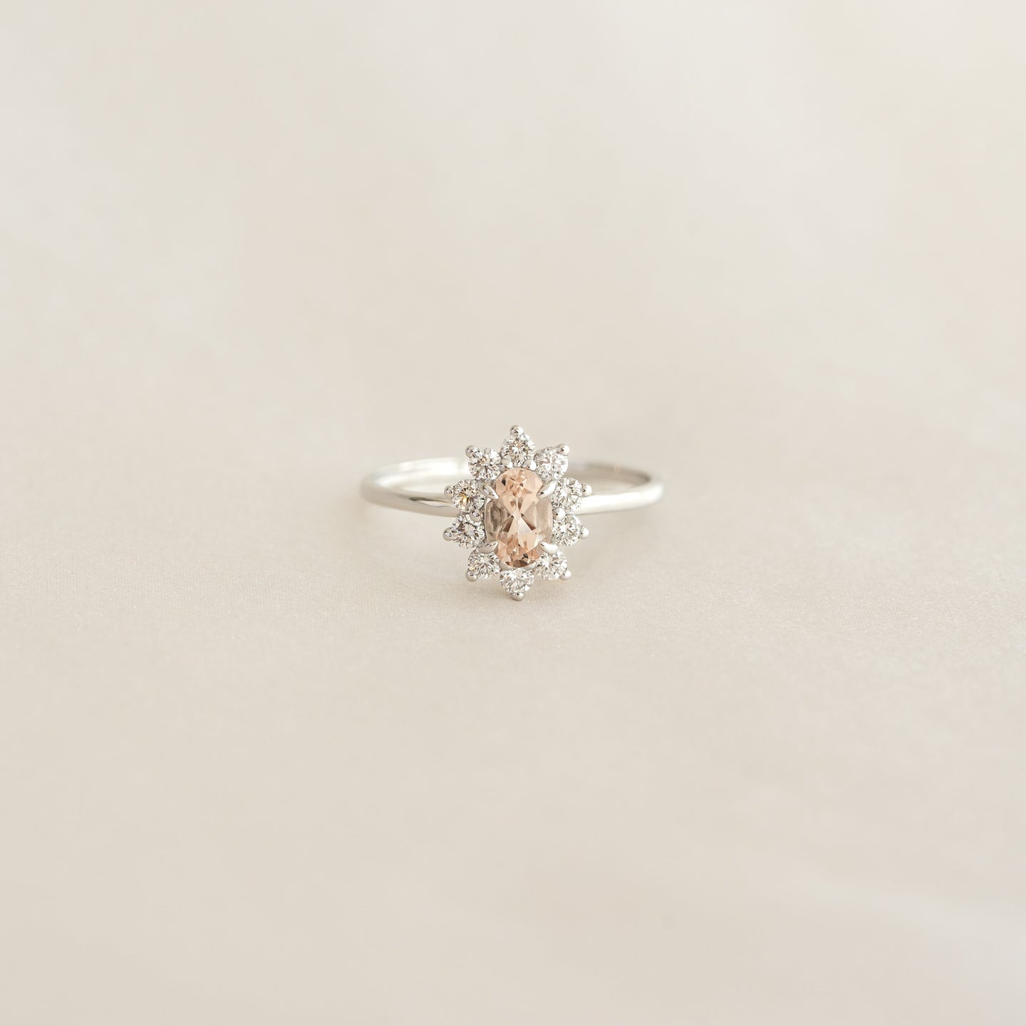 Close-up of Sunburst Morganite Halo Ring White Gold - Evelina with oval morganite and diamond halo on beige background