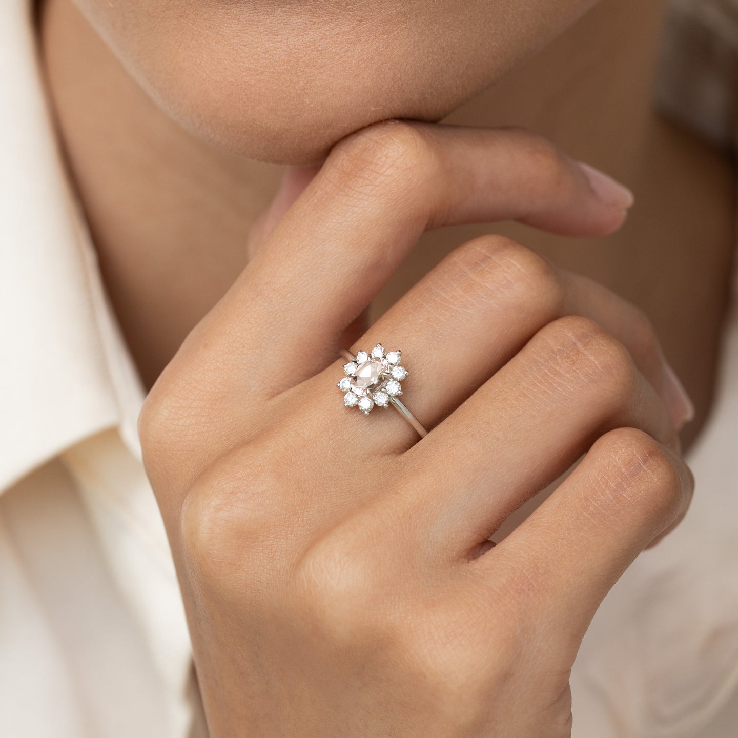 Close-up of hand wearing Sunburst Morganite Halo Ring White Gold - Evelina with an oval center gemstone surrounded by diamonds
