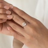 Close-up of hand wearing Sunburst Morganite Halo Ring White Gold - Evelina with oval gemstone and diamond halo on neutral background