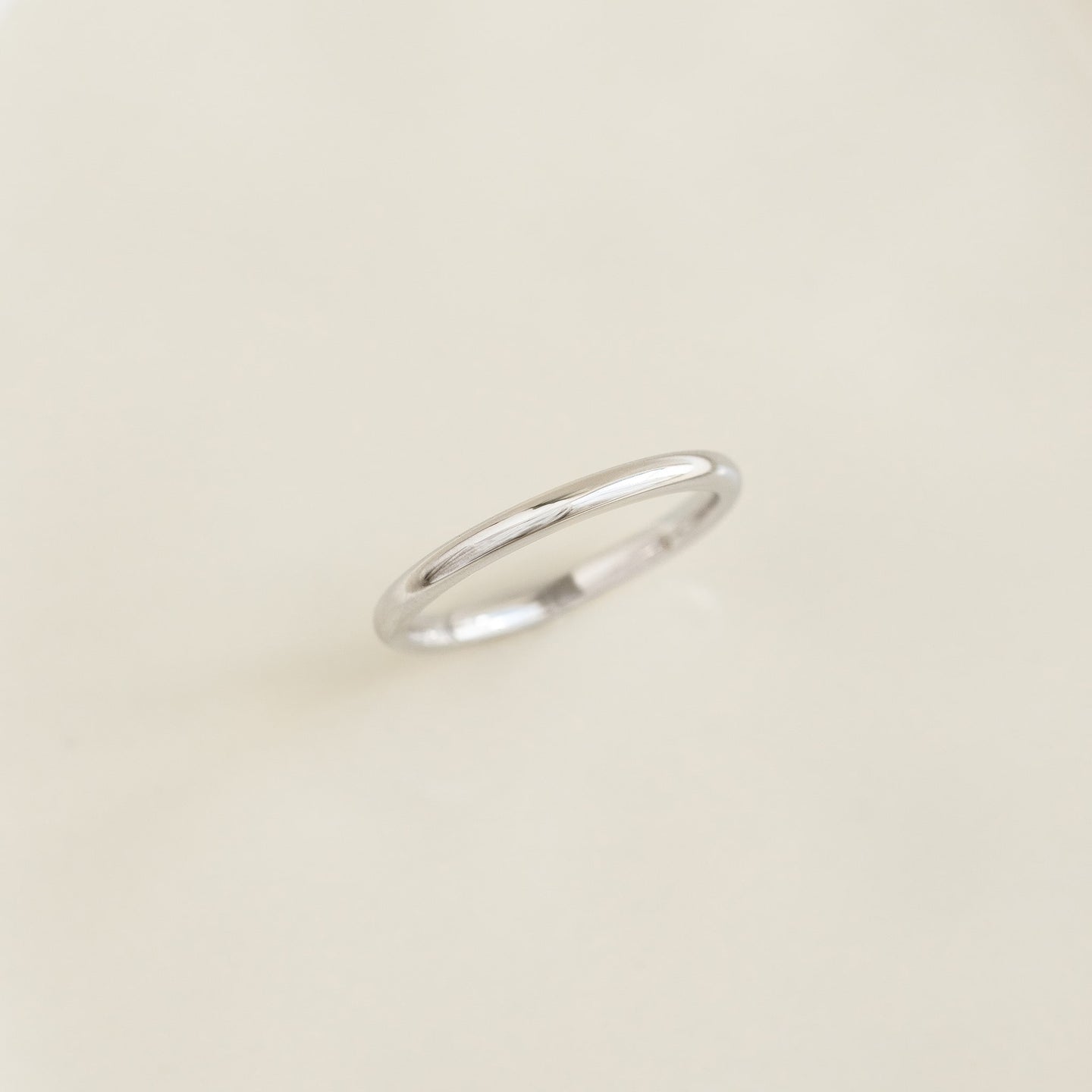 Close-up of a Round White Gold Band - Marni resting on a smooth light beige surface with soft natural lighting
