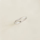 Close-up of a Round White Gold Band - Marni resting on a smooth light beige surface with soft natural lighting